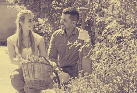Joyful young woman and mature man at the garden with basket of orange flowers