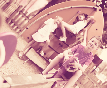 Cheerful boy swinging at playground while his friends playing behindeの写真素材