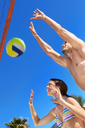 Smiling happy couple playing volleyball on the beachの写真素材