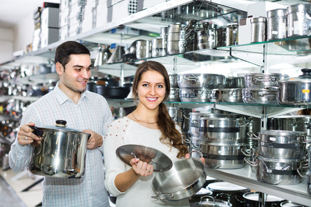 Positive smiling couple in supermarket choosing modern pans in kitchenware sectionの写真素材