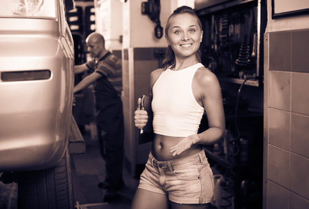 Positive working woman holding cardboard in car workshopの写真素材