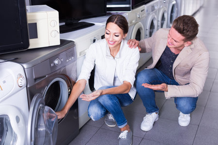 Young couple choosing washing machine in hypermarket and smilingの写真素材