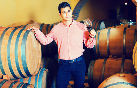 Glad  male customer tasting red wine from wooden barrels in factoryの写真素材