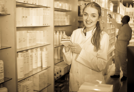 Pharmacist standing at pay desk and male pharmacy technician helpingの写真素材