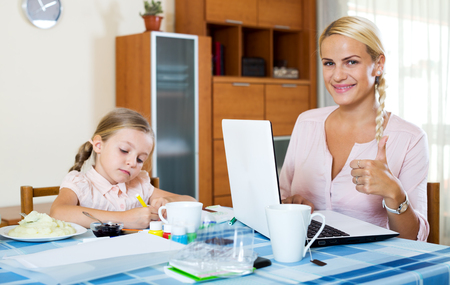 Cheerful woman with daughter working from home using laptop. Focus on woman's handの写真素材