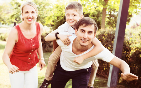 Portrait of cheerful family with boy sitting on father's back hugging each other in parkの写真素材