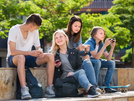 Happy two girls and two boys playing with mobile phones outdoorsの写真素材