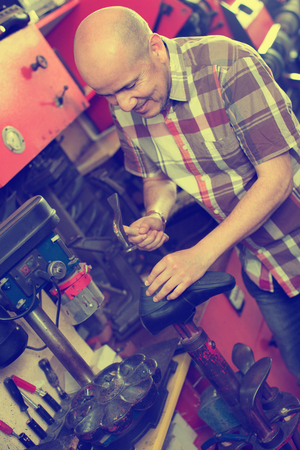 Professional efficient  friendly shoemaker heeling footwear on machine in workshopの写真素材