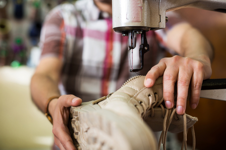 Shoemaker stitching footwear on machine in shoe atelierの写真素材