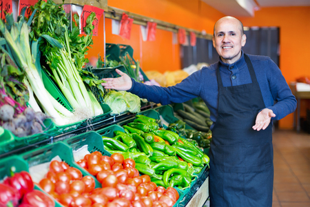 Mature friendly cheerful positive seller offering seasonal vegetables in local groceryの写真素材