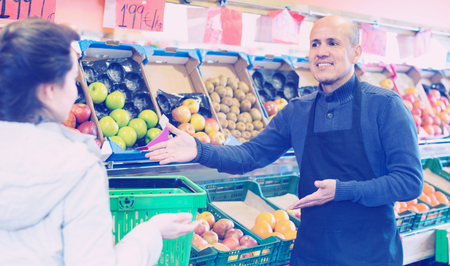 Mature salesman offering female customer assortment of fruitsの写真素材