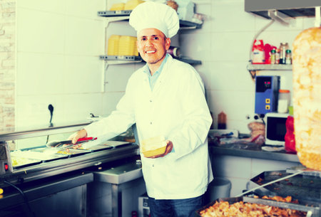smiling mature man chef in uniform serving fresh tasty kebab in restaurant