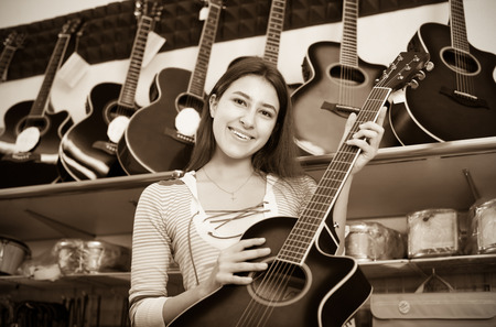 Portrait of young female customer buying new guitar in store and smilingの写真素材
