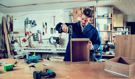 Young glad cheerful positive male worker  finishing to drill drawer at workshopの写真素材