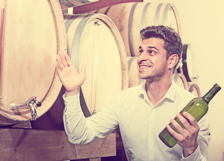 positive smiling man customer buying bottle of wine in shop with woodsの写真素材