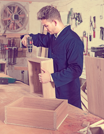 positive working man practising his skills in making drawer at workshopの写真素材