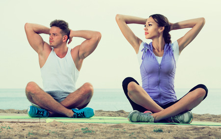 Cross-legged young european  couple practice yoga on beach in morningの写真素材