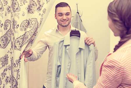 Cheerful young couple with new apparel at fitting-room in clothing storeの写真素材