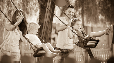 Smiling  mother and father swinging children at park. Focus on womanの写真素材