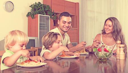 Young smiling family of four eating spaghetti at home interior. Focus on manの写真素材