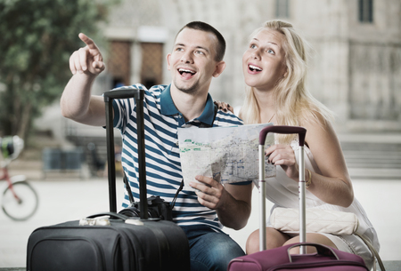 Happy man and charming smiling woman tourists having map and looking for route in cityの写真素材