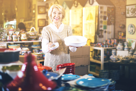 Mature woman selecting ceramic tableware in shop cookwareの写真素材