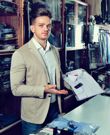 Smiling happy male seller demonstrating shirts in mens cloths storeの写真素材