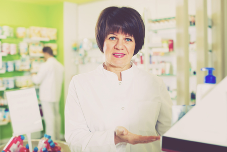 smiling woman pharmacist wearing uniform and working and helping in pharmaceutical shopの写真素材
