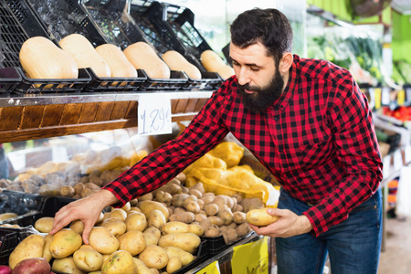 Glad cheerful positive male seller offering potatoes in grocery shopの写真素材