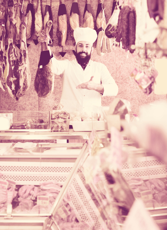 Cheerful young male seller offering displayed jamon in butchers shopの写真素材