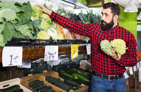 Young glad positive male seller offering cauliflowers in grocery shopの写真素材