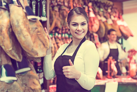 happy russian female brunette selling jamon and smiling in delicatessen storeの写真素材