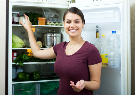 Portrait happy woman standing near filled fridge at homeの写真素材