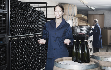 cheerful adult man and women coworkers looking at bubbly wine in bottle standing in wine cellarの写真素材