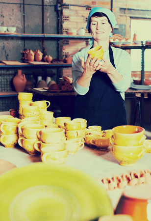 Portrait of an elderly woman displaying cups at the workshopの写真素材