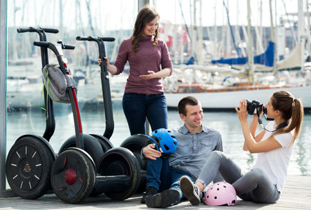 Positive company of  friends sitting near segways at sea front and smiling