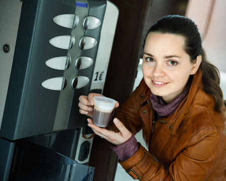 Smiling pleasant  woman buying coffee from automatic machineの写真素材