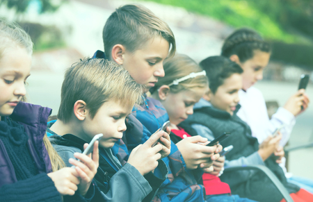 Outdoor portrait of little girls and boys playing with phonesの写真素材
