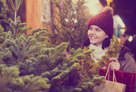 Adult girl staying at market among Christmas treesの写真素材