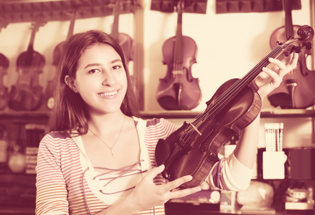 Happy longhaired girl choosing full size violin in music shopの写真素材