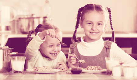 Two small cheerful girls eating healthy oatmeal at home kitchenのeditorial素材