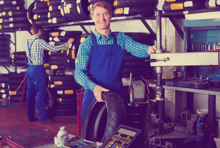 Handsome working man standing with new tires for motorbike in hands in workshopのeditorial素材