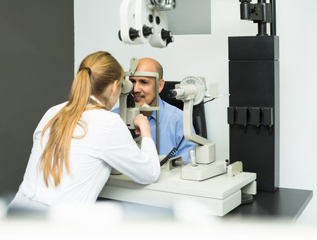 Friendly female ophthalmologist and happy european mature patient checking eyesight in clinicの写真素材