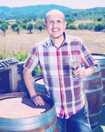 Smiling positive glad mature man holding glass with sparkling wine outdoors on terrace with wine woodsの写真素材