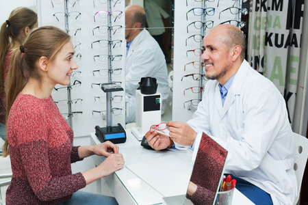 Positive senior male optician offering glasses frames to young smiling womanの写真素材