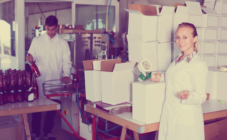Happy woman in uniform packing wine bottles on winery factoryの写真素材
