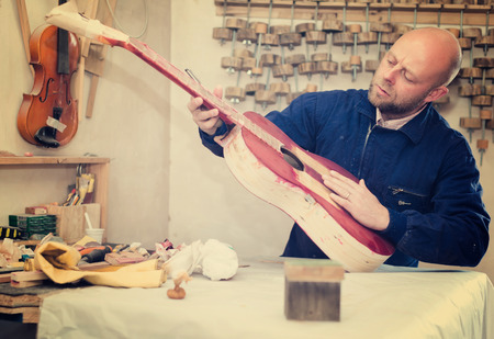 Skilled guitar-maker working with unfinished guitar at workshopの写真素材