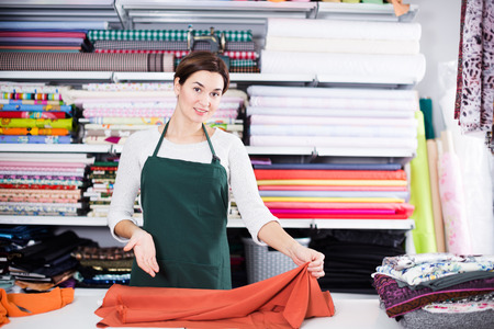 Smiling girl seller taking measurement of cloth at drapery shopの写真素材
