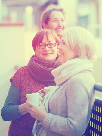 Portrait of cheerful female pensioners drinking coffee at patio. Focus on brunetteの写真素材