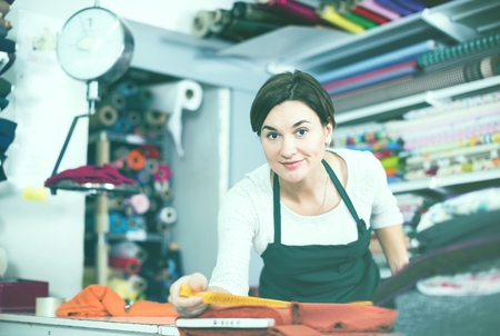 Smiling girl seller taking measurement of cloth at drapery shopの写真素材